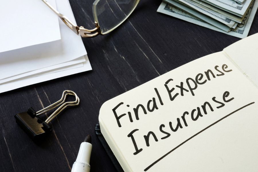 A notebook reads "Final Expense Insurance" with glasses, papers, and cash nearby on a dark surface.